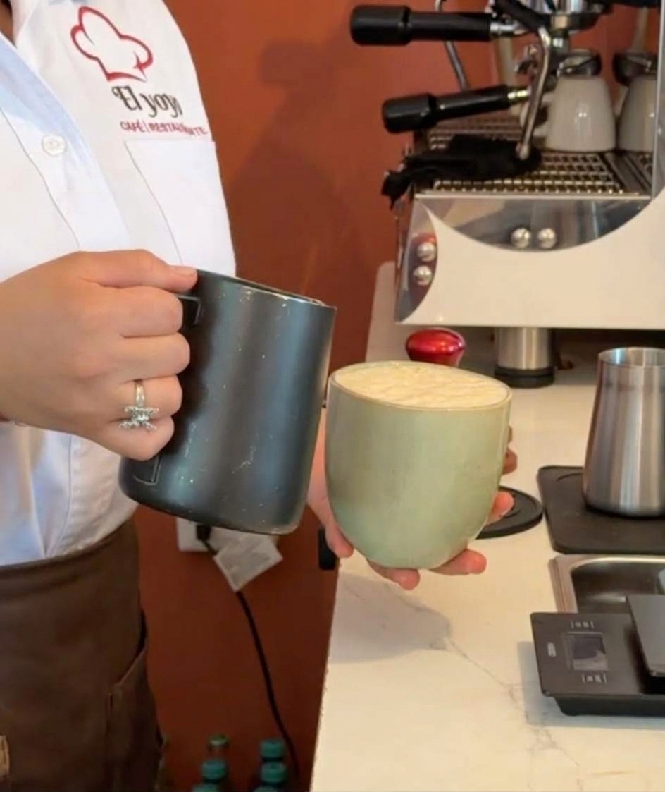 Barista de Cafetería El Yoyo sirviendo una bebida en taza verde